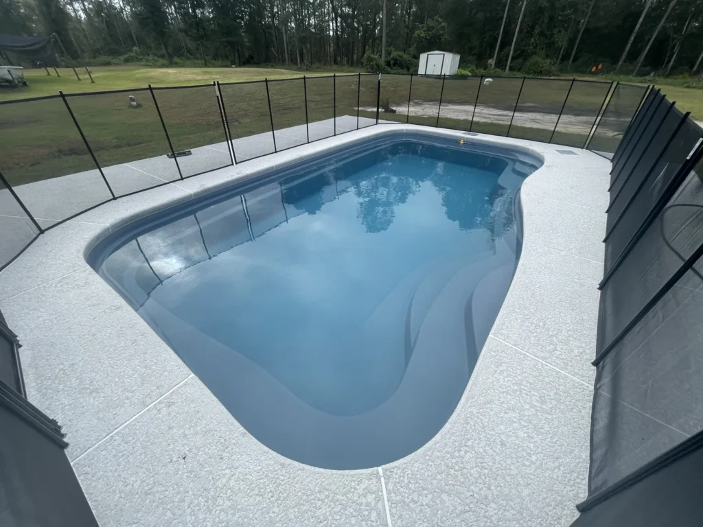 Wide view of a finished fiberglass pool, deck and safety fence