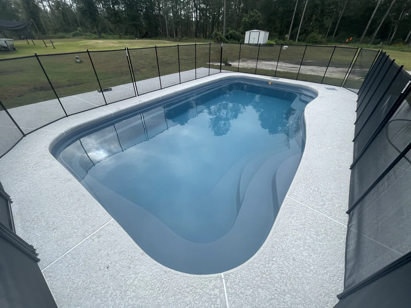 Wide view of a finished fiberglass pool, deck and safety fence