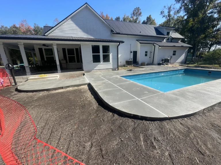 Freshly poured concrete deck curing around a new fiberglass pool