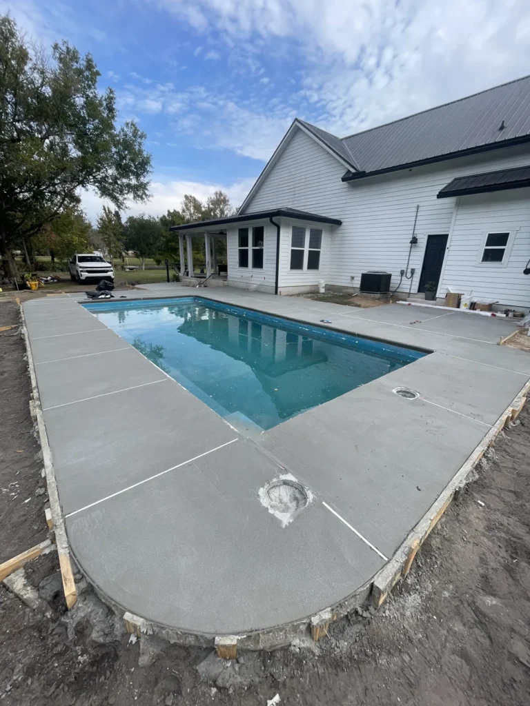 Finished fiberglass pool with blue water beside a newly built home