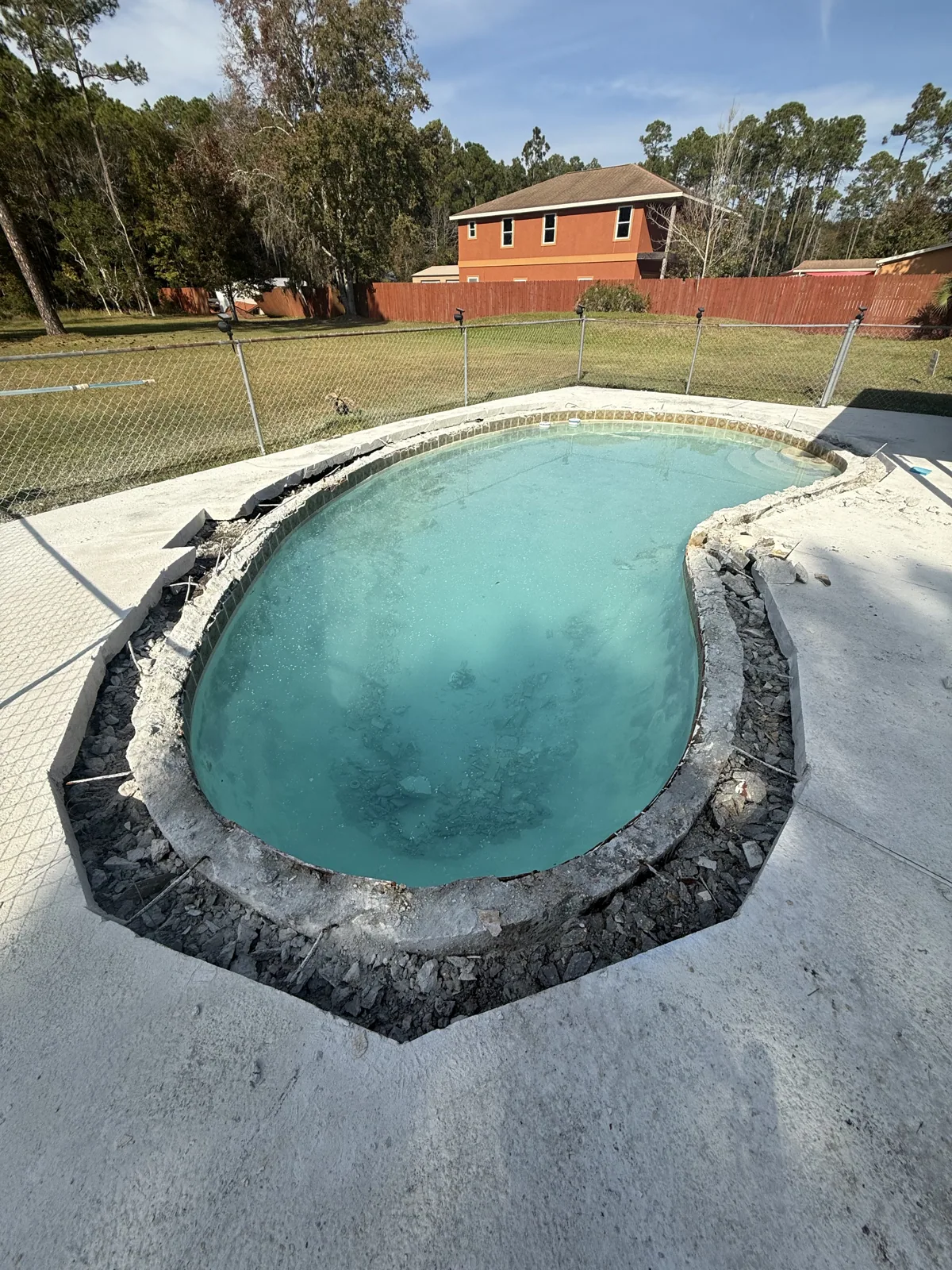 Aging kidney-shaped concrete pool before remodeling, with failing rock coping and a worn deck
