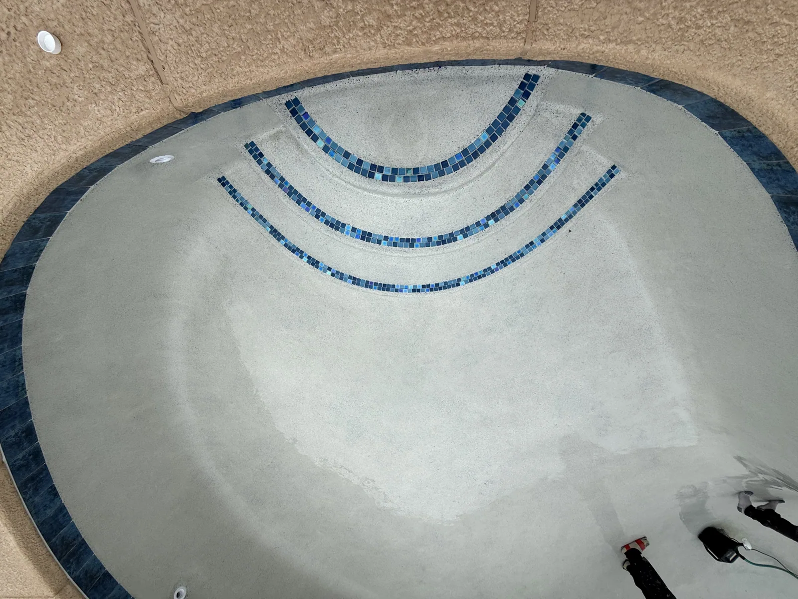 Blue mosaic waterline tile and step detail on a newly plastered pool