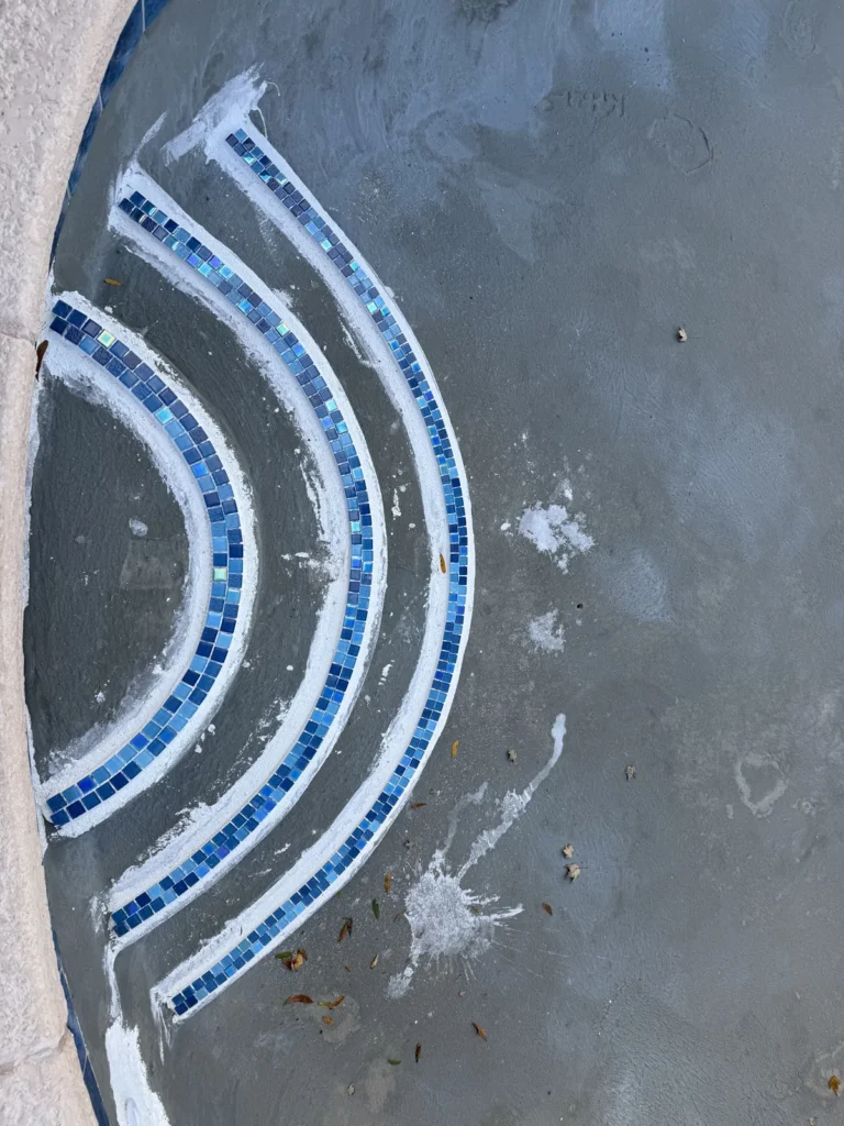 Close view of curved blue mosaic tile bands on freshly finished pool steps